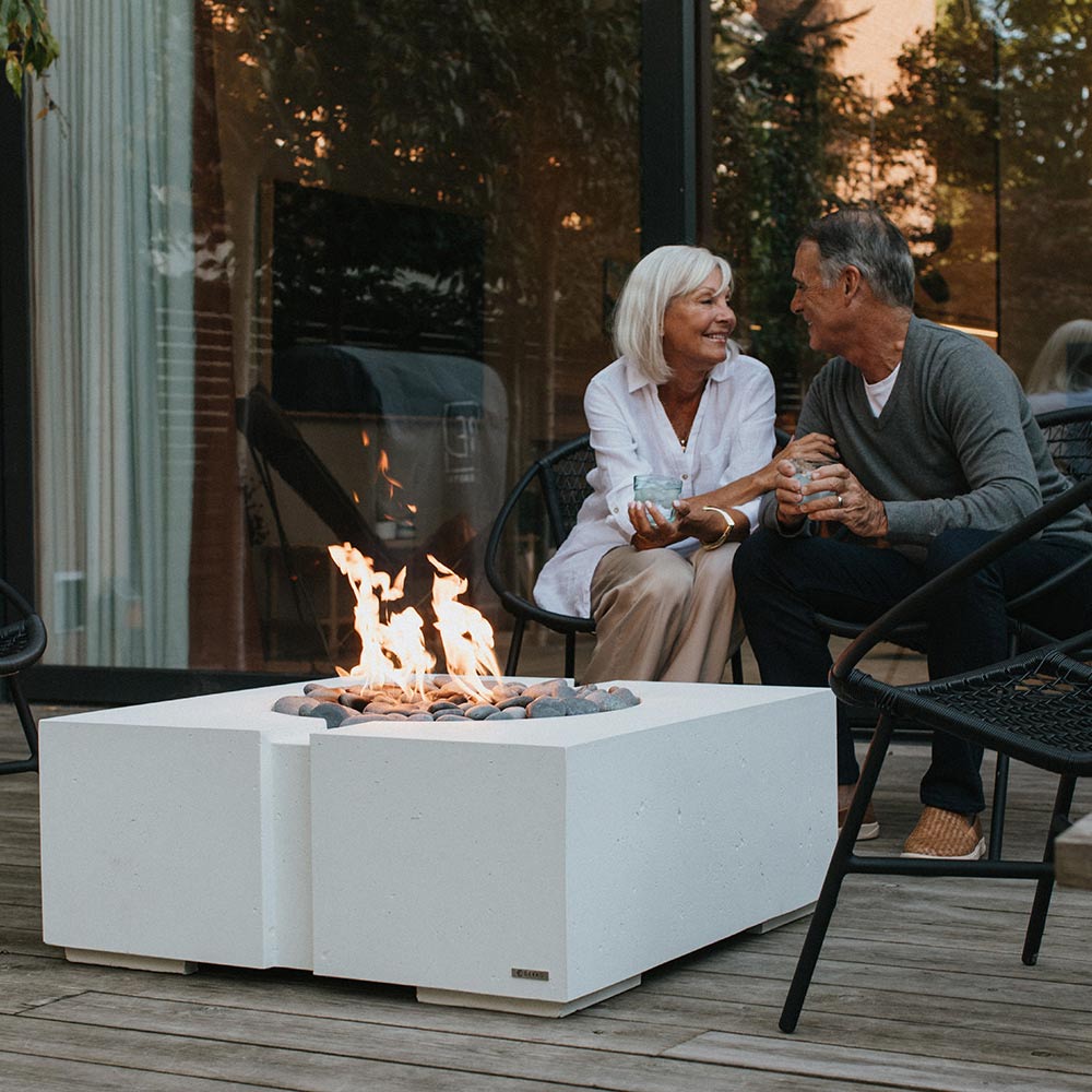 Square concrete gas fire pit with flame and stone filler on outdoor patio flooring