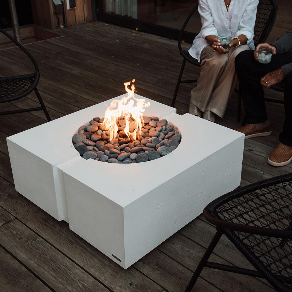Square concrete gas fire pit with flame over gray rocks on a wooden deck