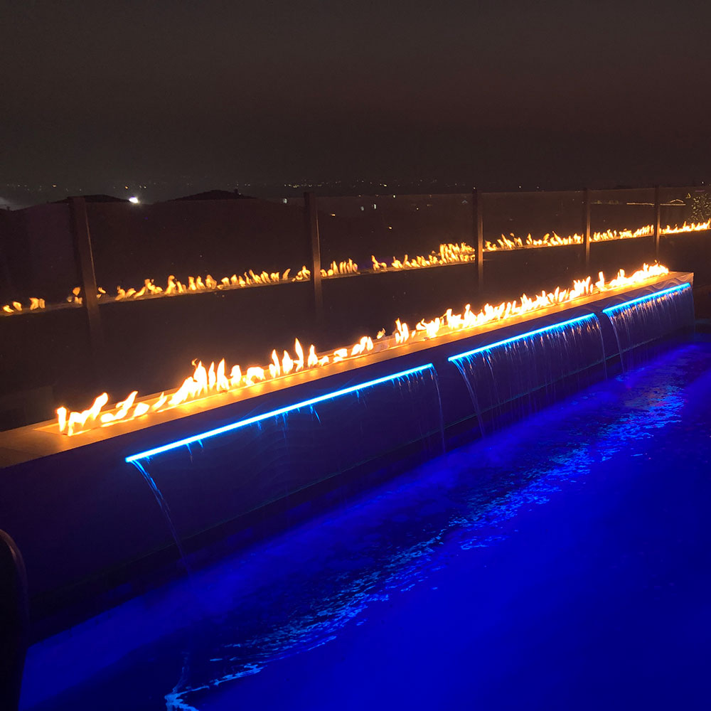 Linear gas fire pit burner producing a steady row of flames along the trough
