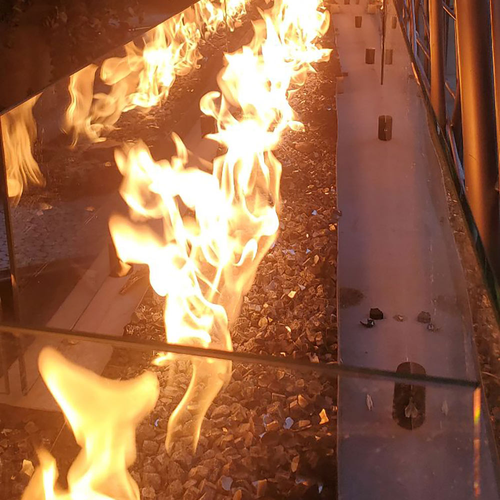 Linear gas fire pit burner with high flames shooting from the metal trough
