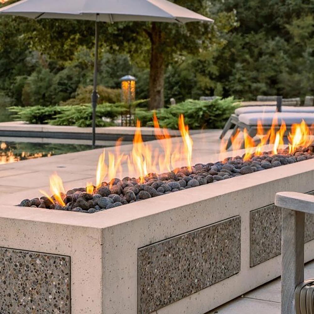 Outdoor linear gas fire pit burner in a stone trough, with flames over lava rocks