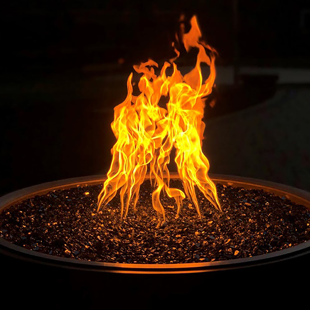Flaming gas fire pit burner with bright orange flames rising from a dark firebed