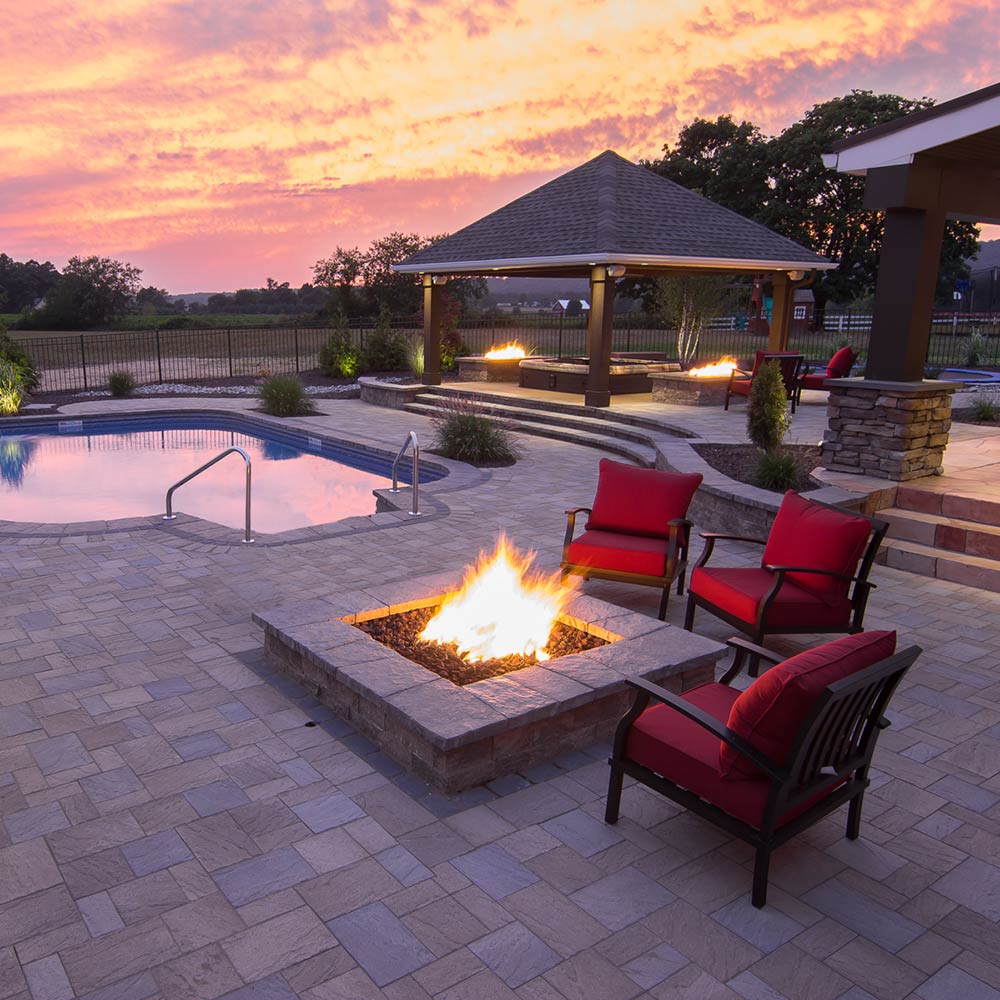 Outdoor gas fire pit with flames in a square stone bowl and burner head