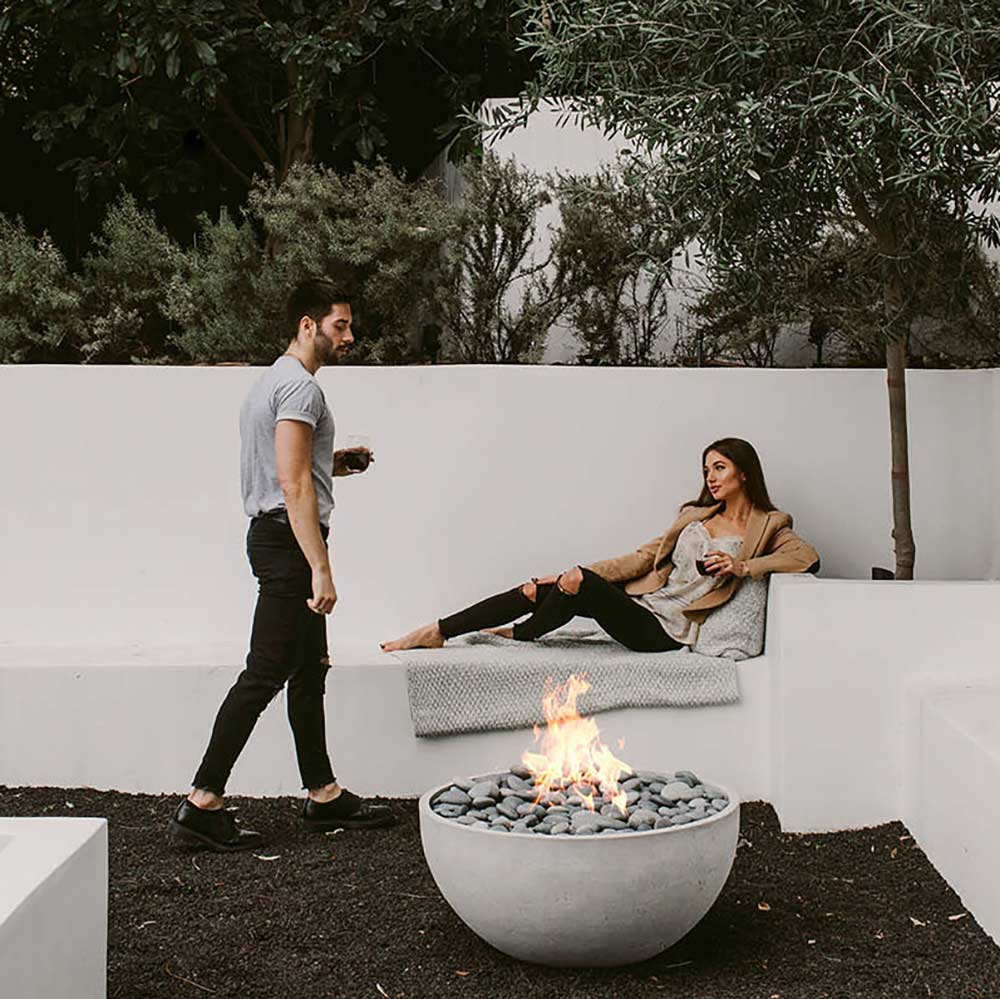 Concrete outdoor gas fire bowl with burning flames and gray stones on patio
