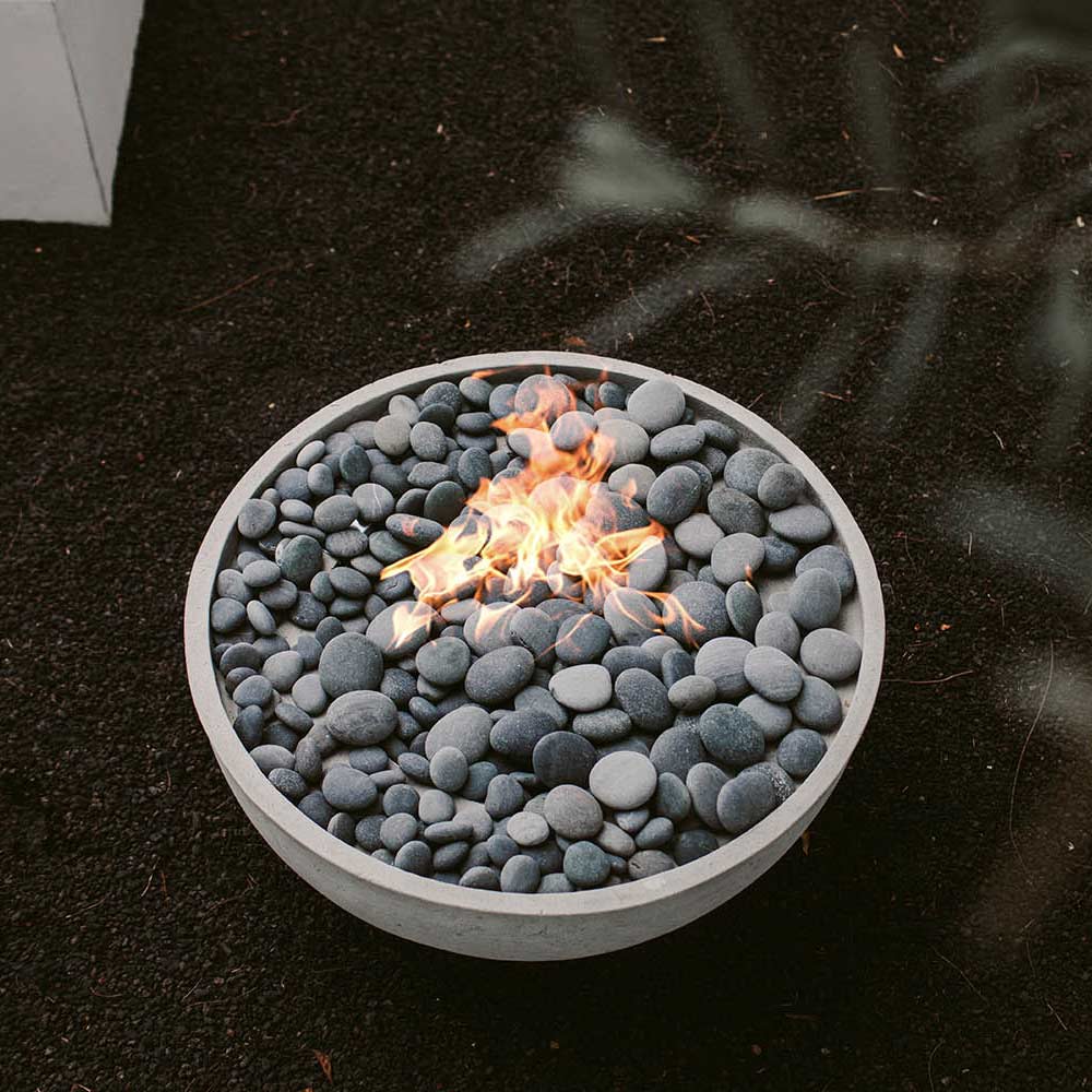 Round concrete gas fire bowl with flames surrounded by gray decorative stones