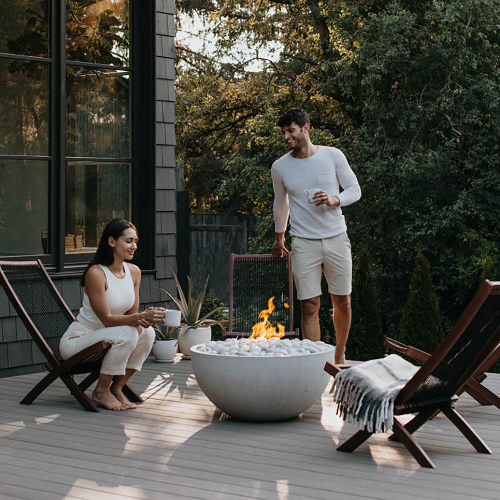 Concrete gas fire bowl with small flames and pale gray stones on patio