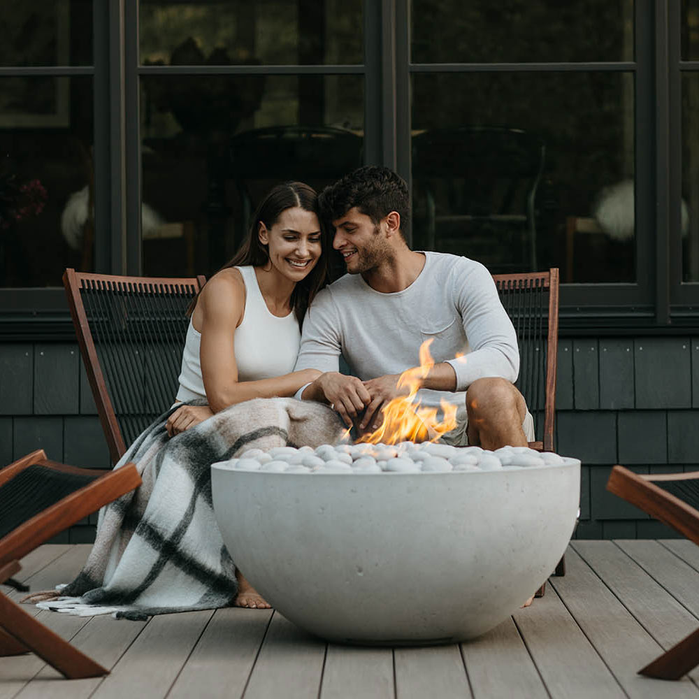 Round concrete gas fire bowl with flames over gray decorative stones
