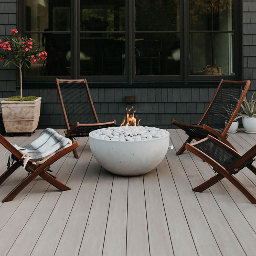Outdoor concrete gas fire bowl with flames and light gray stones on patio