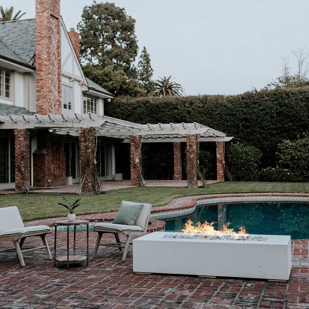 Lightweight concrete gas fire pit with flames on a patio near outdoor seating.