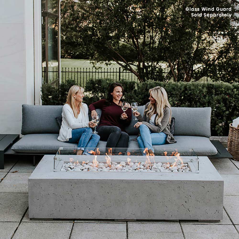 Lightweight concrete gas fire pit with glass wind guard across the open flame bed.