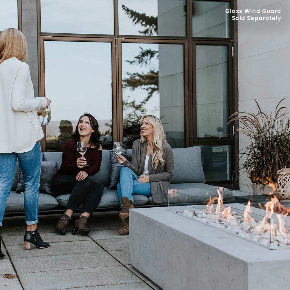 Lightweight concrete gas fire pit with a glass wind guard around the flame bed.