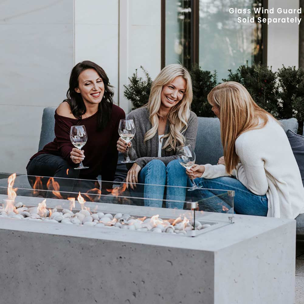 Lightweight concrete gas fire pit with glass wind guard and visible flames along the center.