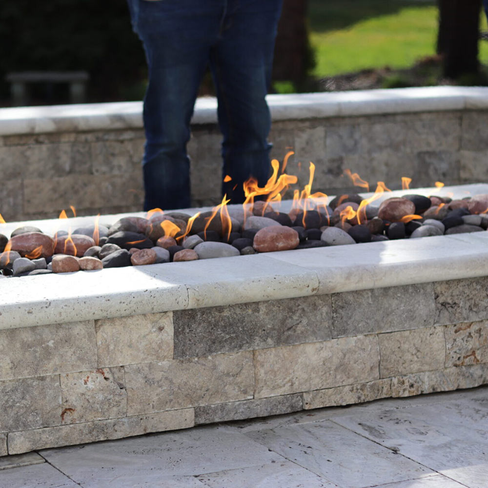 Outdoor gas fire pit with flames burning over river rocks in a stone surround