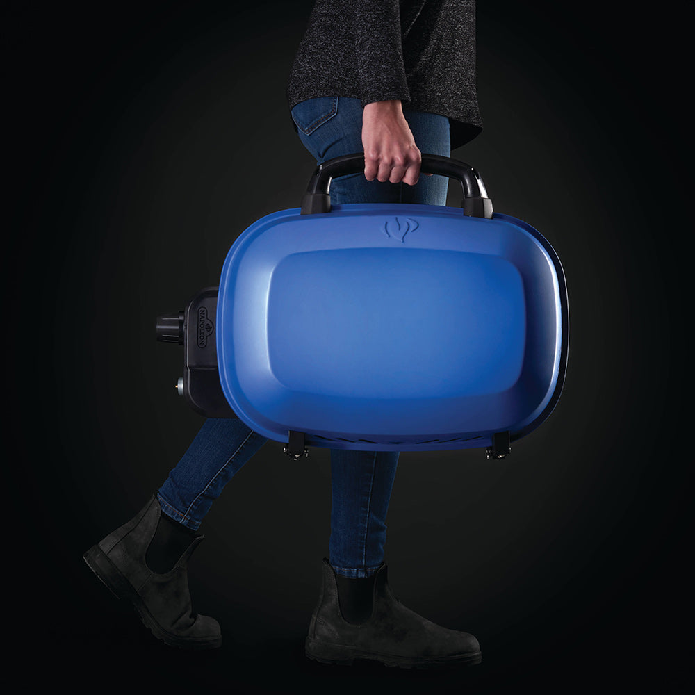 Blue portable gas grill carried by handle with lid closed and side control port visible