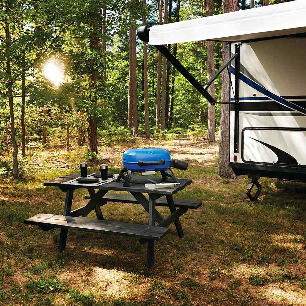Blue portable gas grill on outdoor table with lid closed and black side burner controls