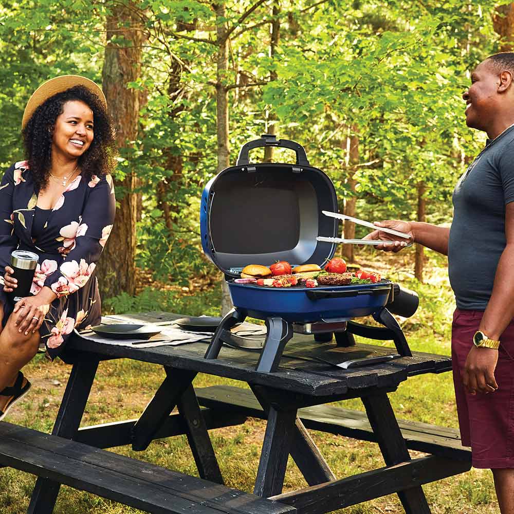 Blue portable gas grill open on outdoor table with food on cooking grate