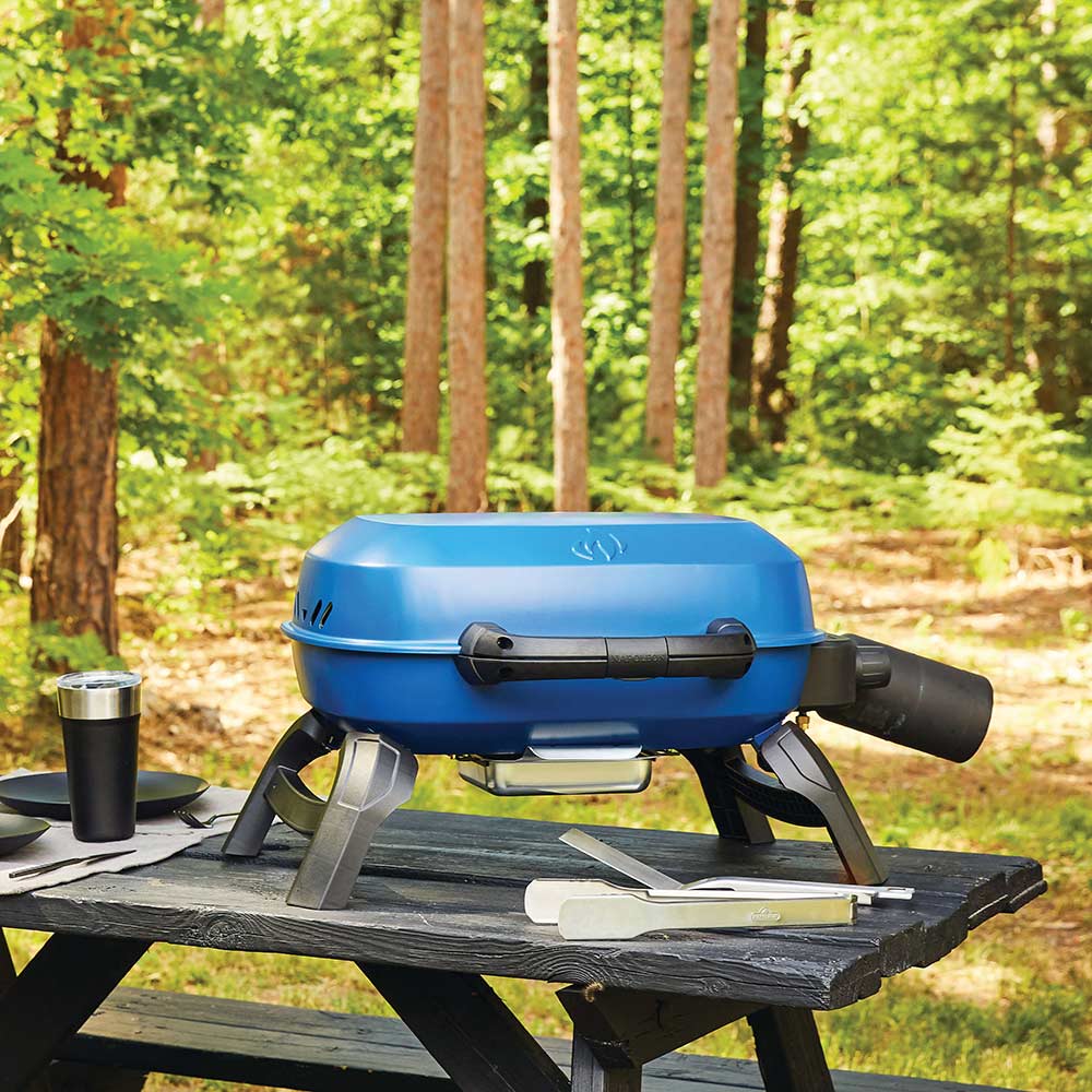 Blue portable tabletop gas grill with lid closed on outdoor table