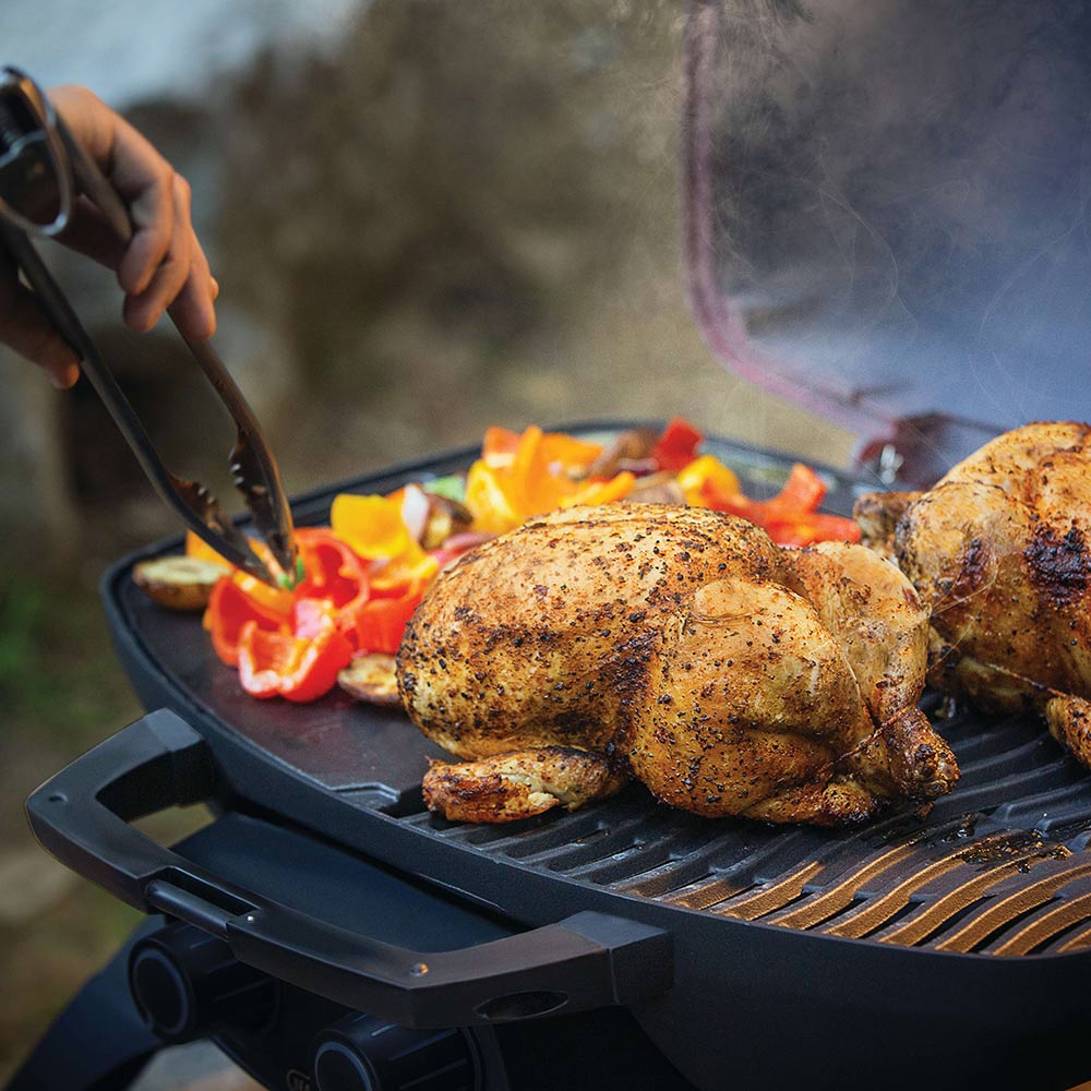 Portable gas grill with seasoned whole chicken cooking over open grates