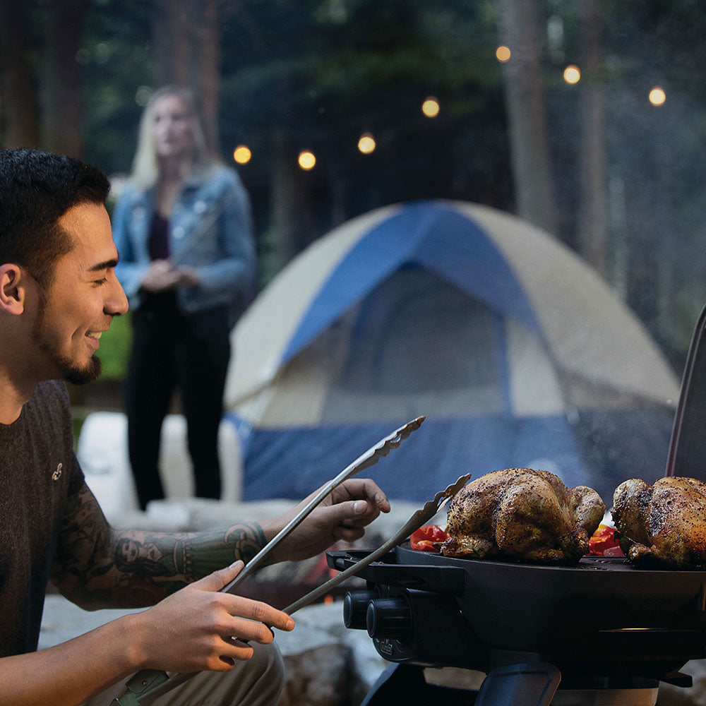Portable tabletop gas grill with roasted chicken cooking outdoors at night