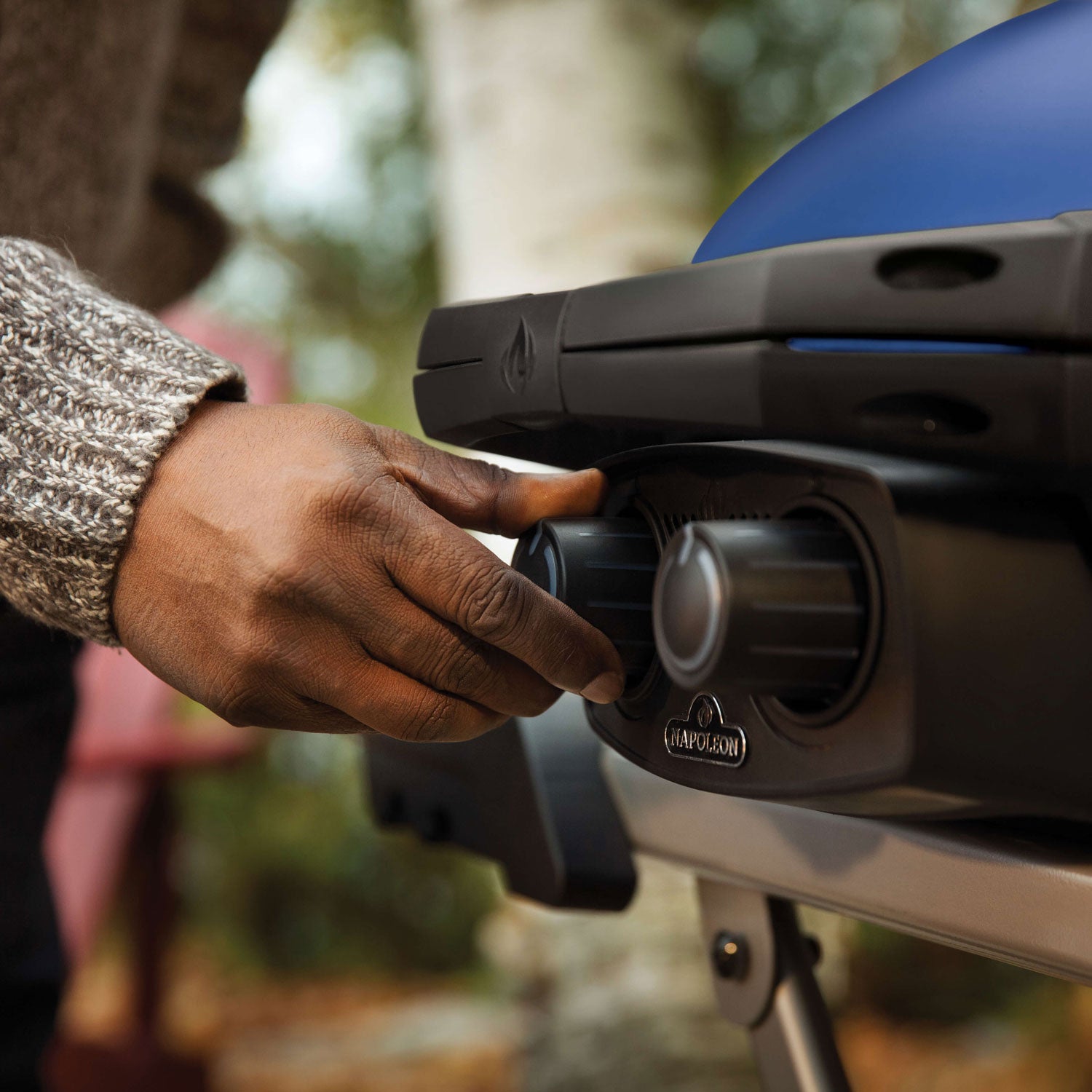 Hand turning a control knob on a portable propane grill with blue lid and black body