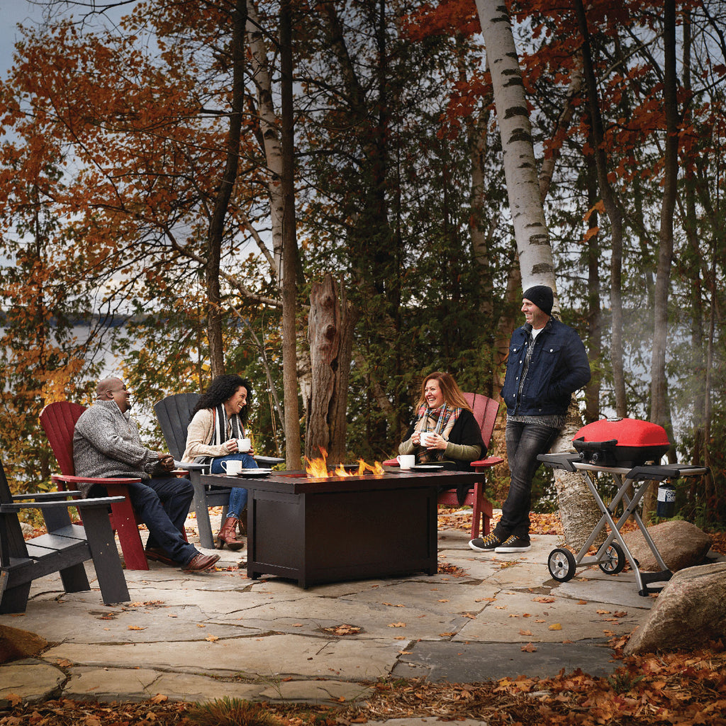 Portable propane grill on a scissor cart with people gathered outdoors