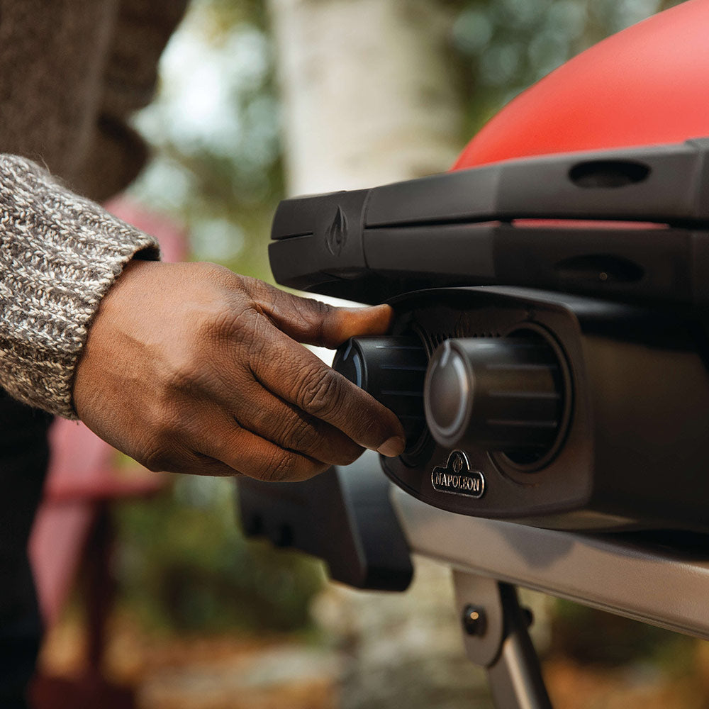 Hand adjusting a control knob on a red portable propane grill.