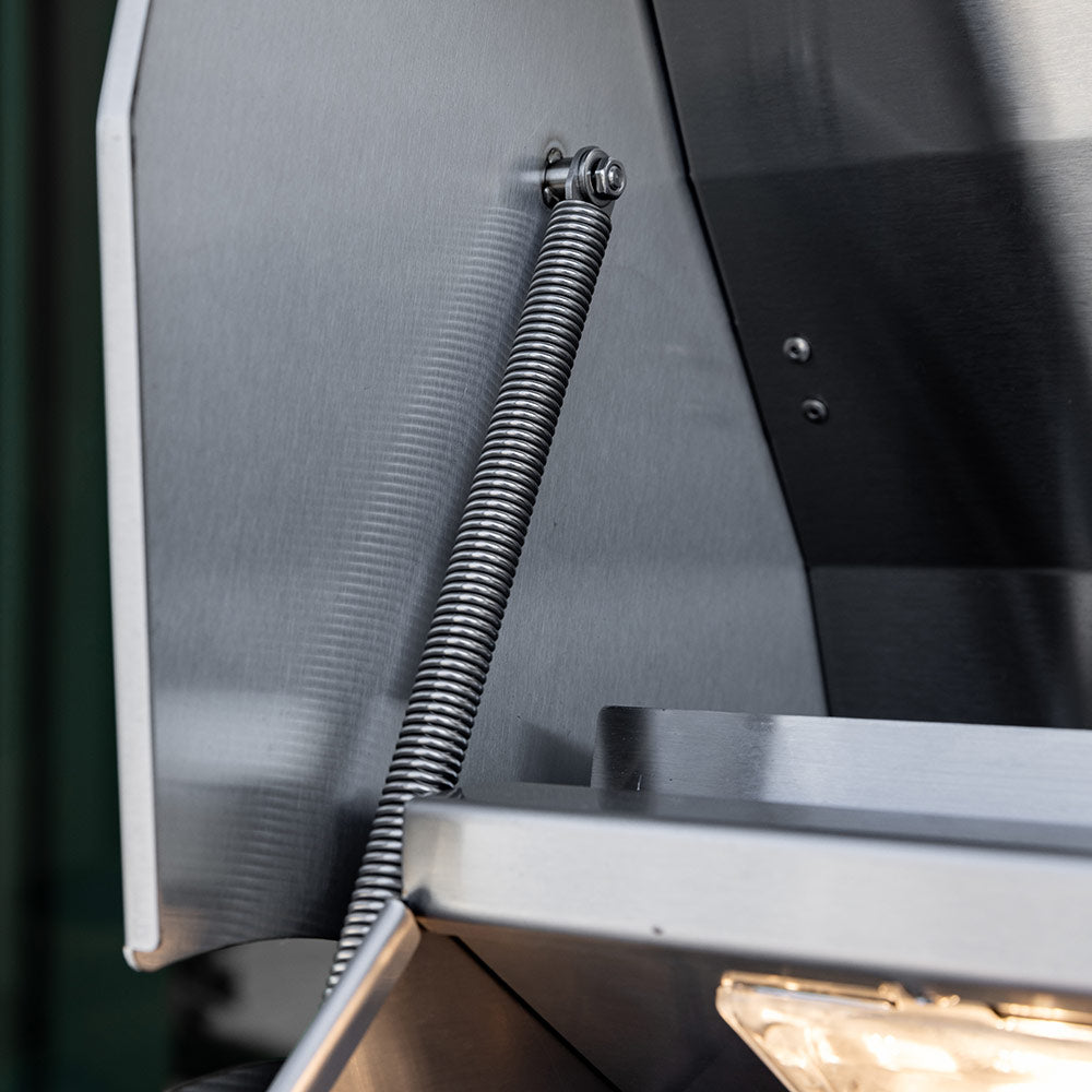 Gas grill interior panel with braided gas line and spring detail, close-up