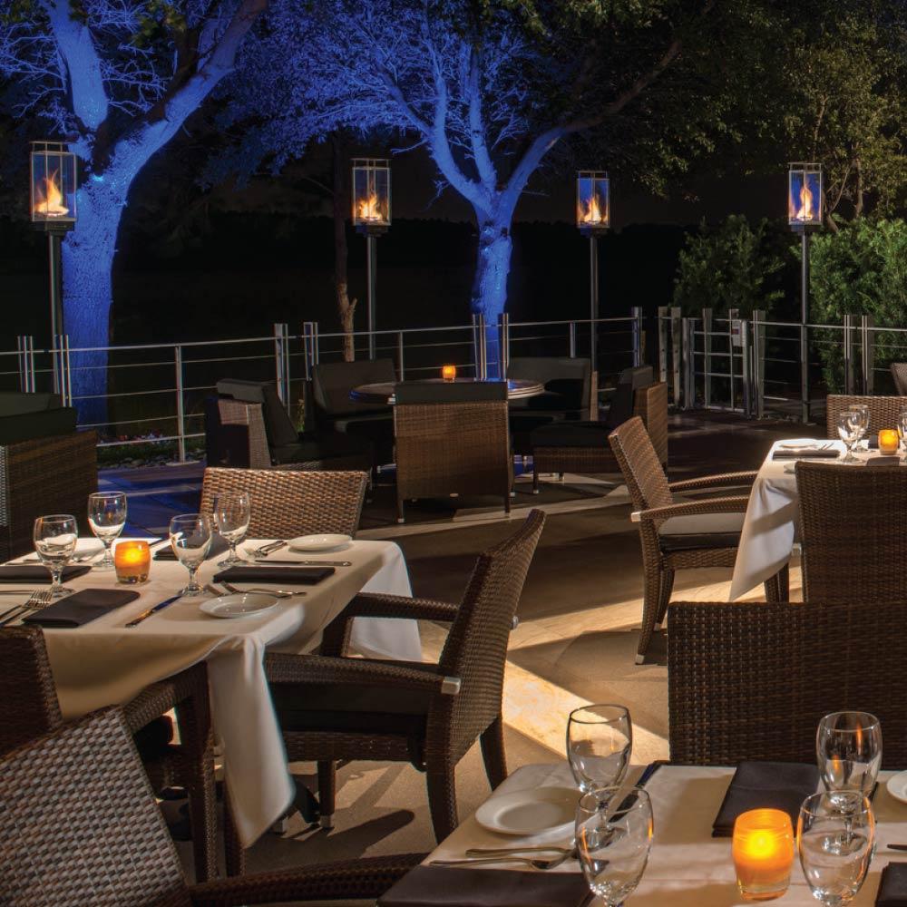 Outdoor patio dining set with multiple black gas torches emitting flames