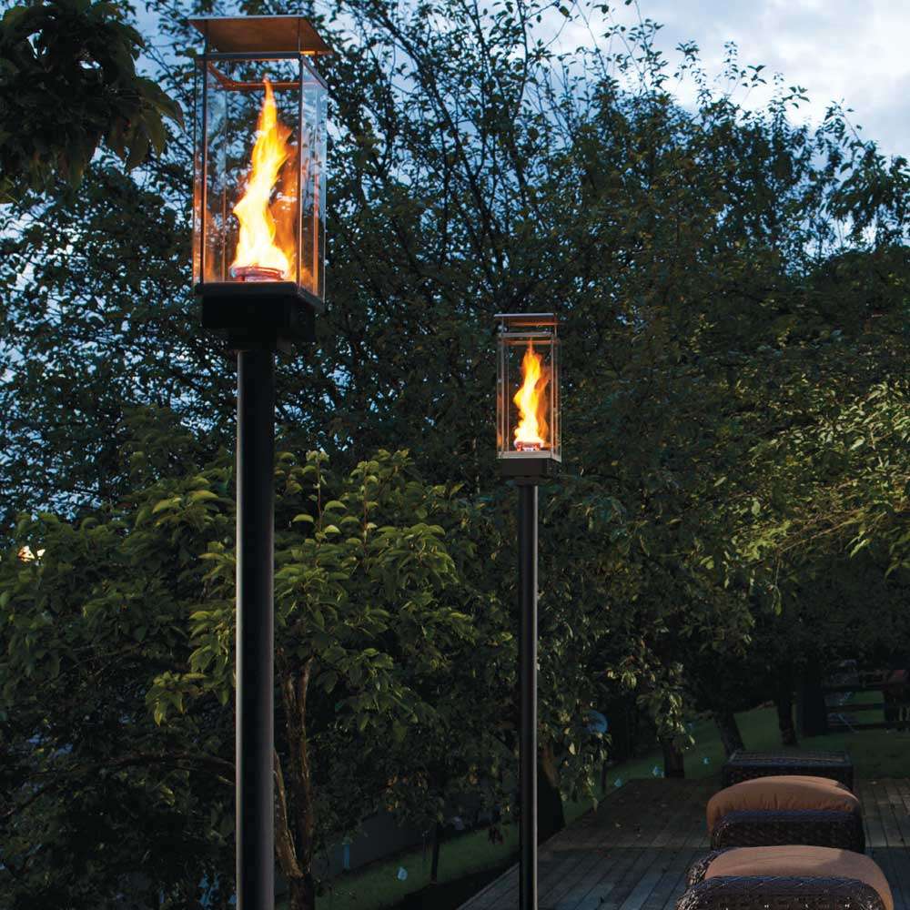 Two Tempest Torch gas lanterns with clear glass and orange flames on tall posts