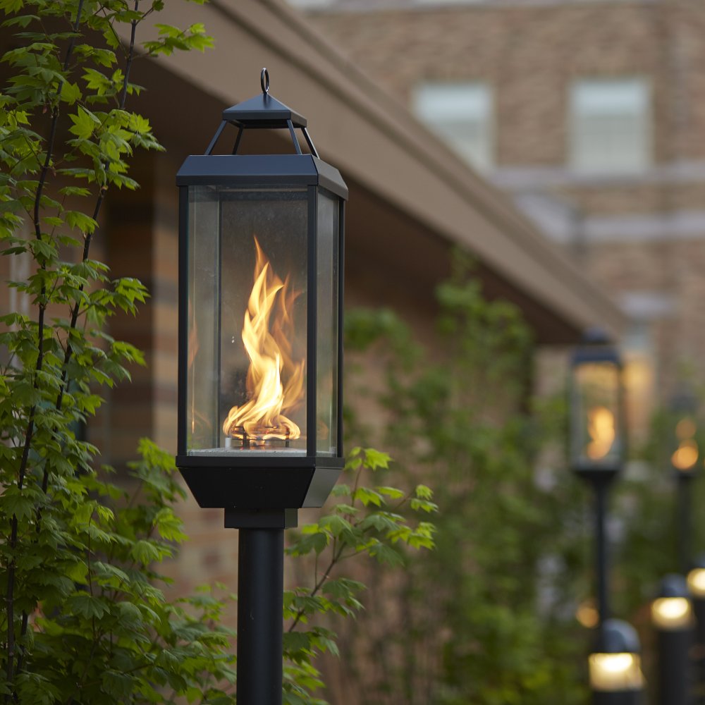 Black gas lantern on post with burning flame inside clear glass panels