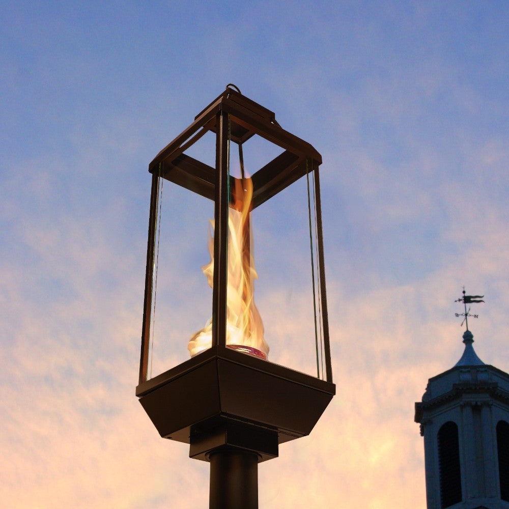 Outdoor black gas lantern on post with visible flame through glass panels