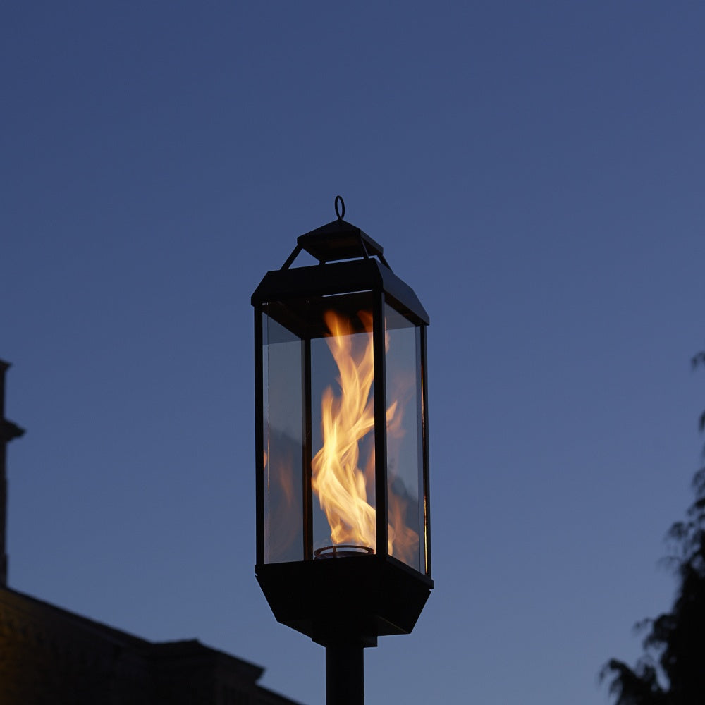 Black gas lantern with flame in glass enclosure on a post mount