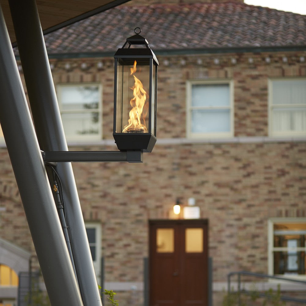 Black gas wall lantern with glass panels and burning flame, mounted bracket visible