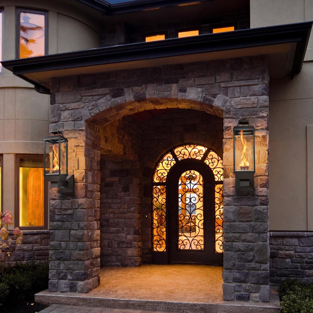 Black gas lantern with glass enclosure and burning flame, mounted on stone wall