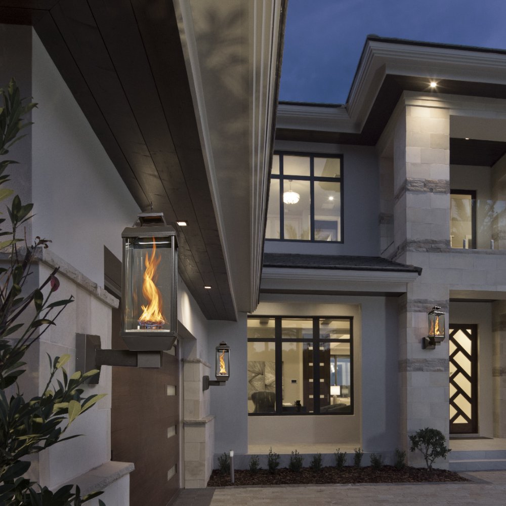 Wall-mounted gas lantern with glass sides and burning flame on exterior patio