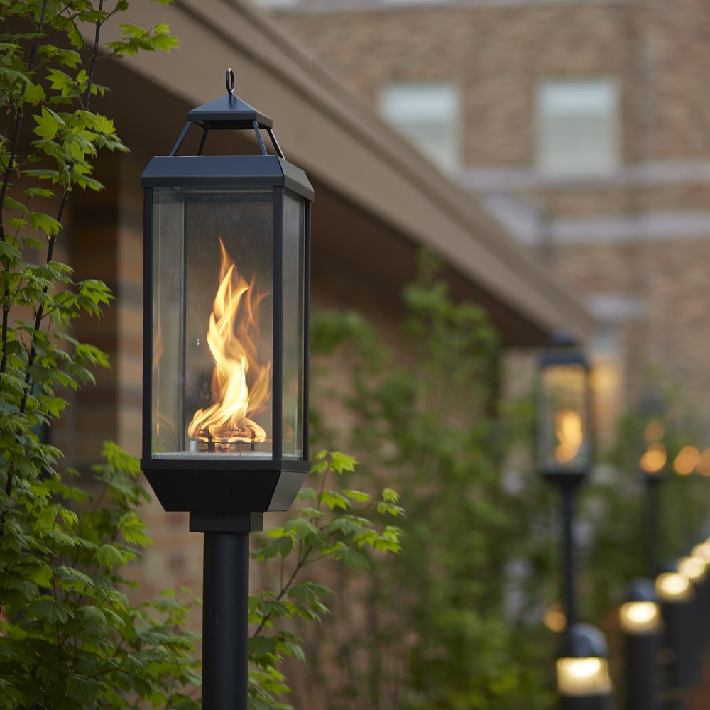 Outdoor gas lantern on a dark post with glowing flame behind glass