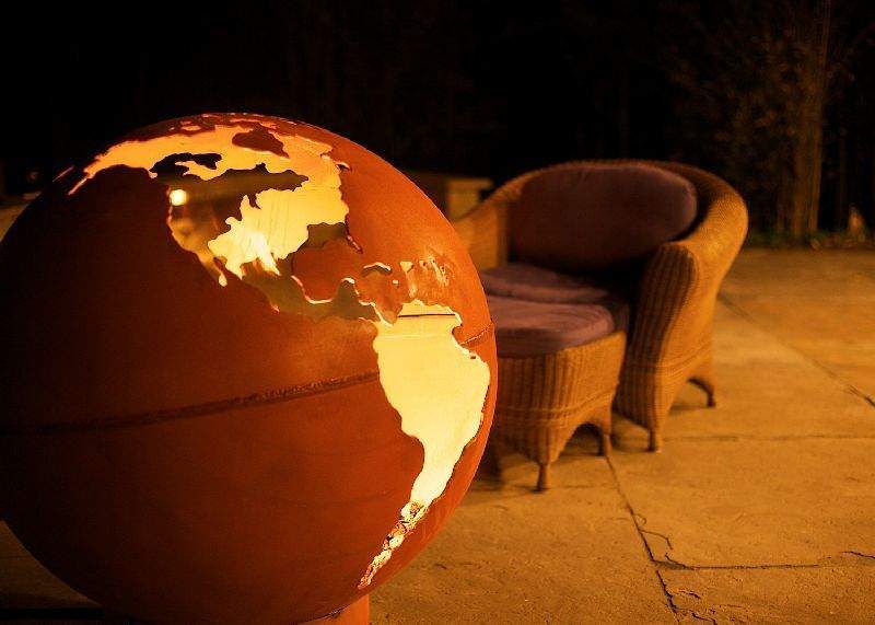 Globe gas fire pit with orange globe and flames glowing inside continent cutouts
