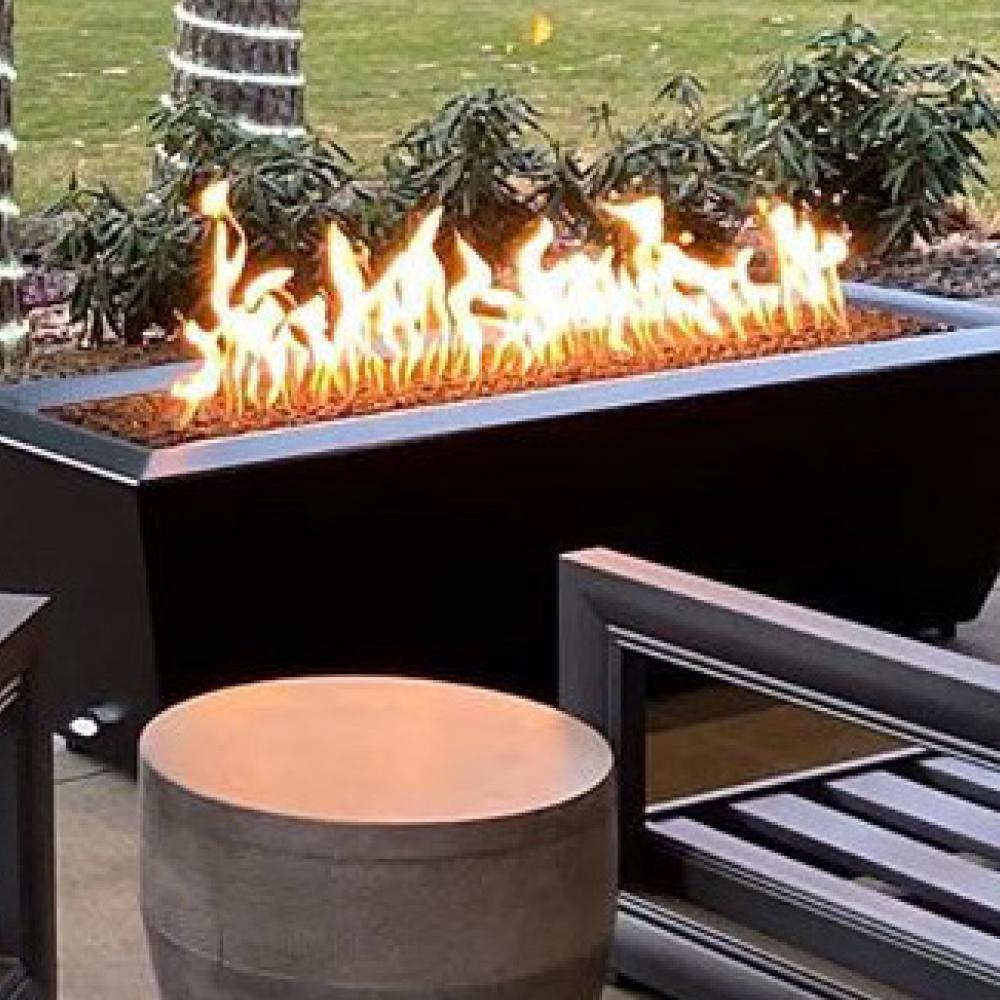 Linear gas burner producing flames at a patio fire pit