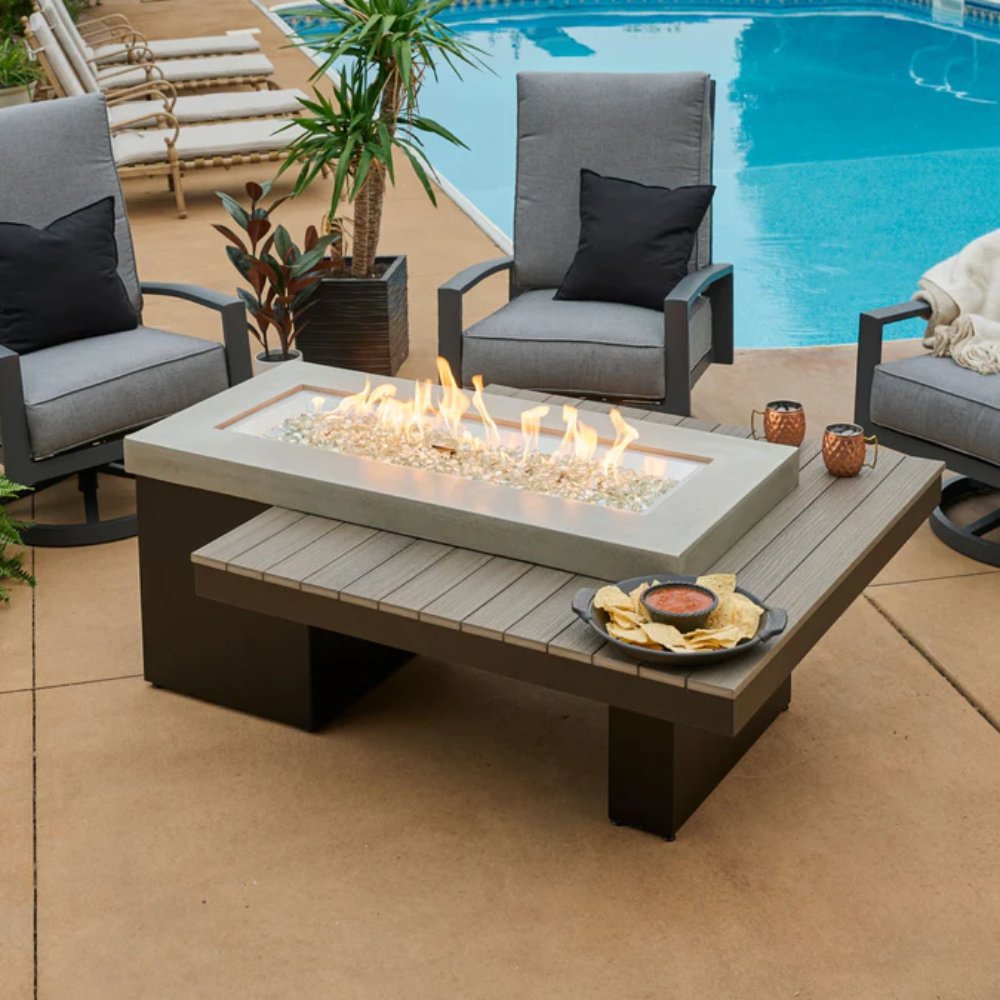 Linear gas fire pit table with glowing flames and beige stone surround