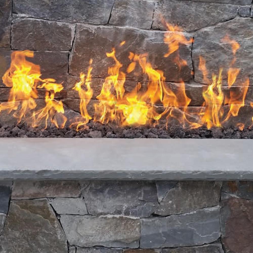 Electronic ignition burner producing orange flames along a stone fireplace ledge