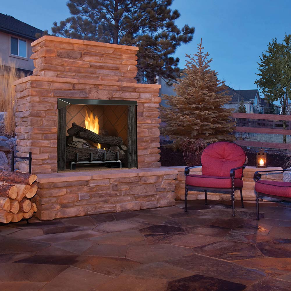 Outdoor gas firebox in stone surround with burning logs and black firebox frame