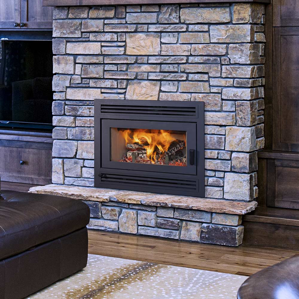 Black wood-burning fireplace with glass door and lit fire, stone wall