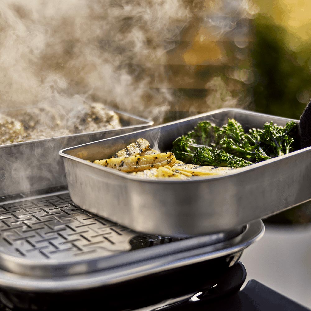 Stainless grill insert pan with vegetables on a hot grill