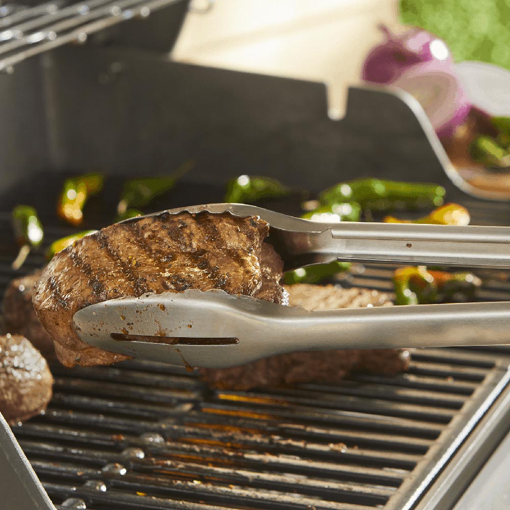 Grill tongs gripping a grilled meat patty on metal grates