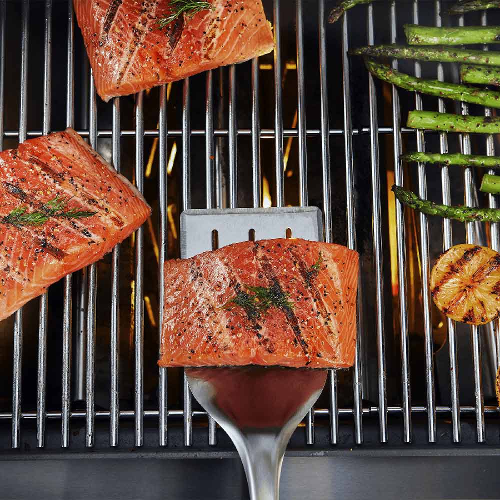 Grill spatula with stainless head holding salmon on hot grates