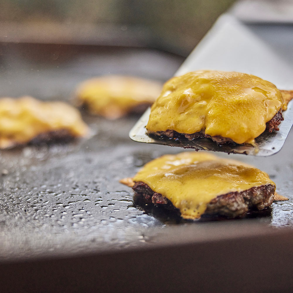 Griddle spatula lifting a cheeseburger on a hot griddle