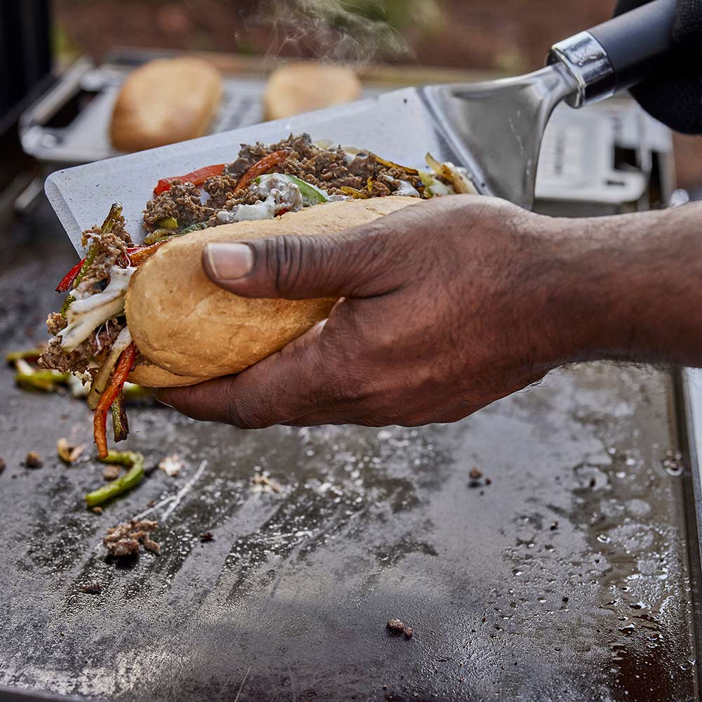 Griddle spatula lifting a sandwich on a hot griddle, held in hand