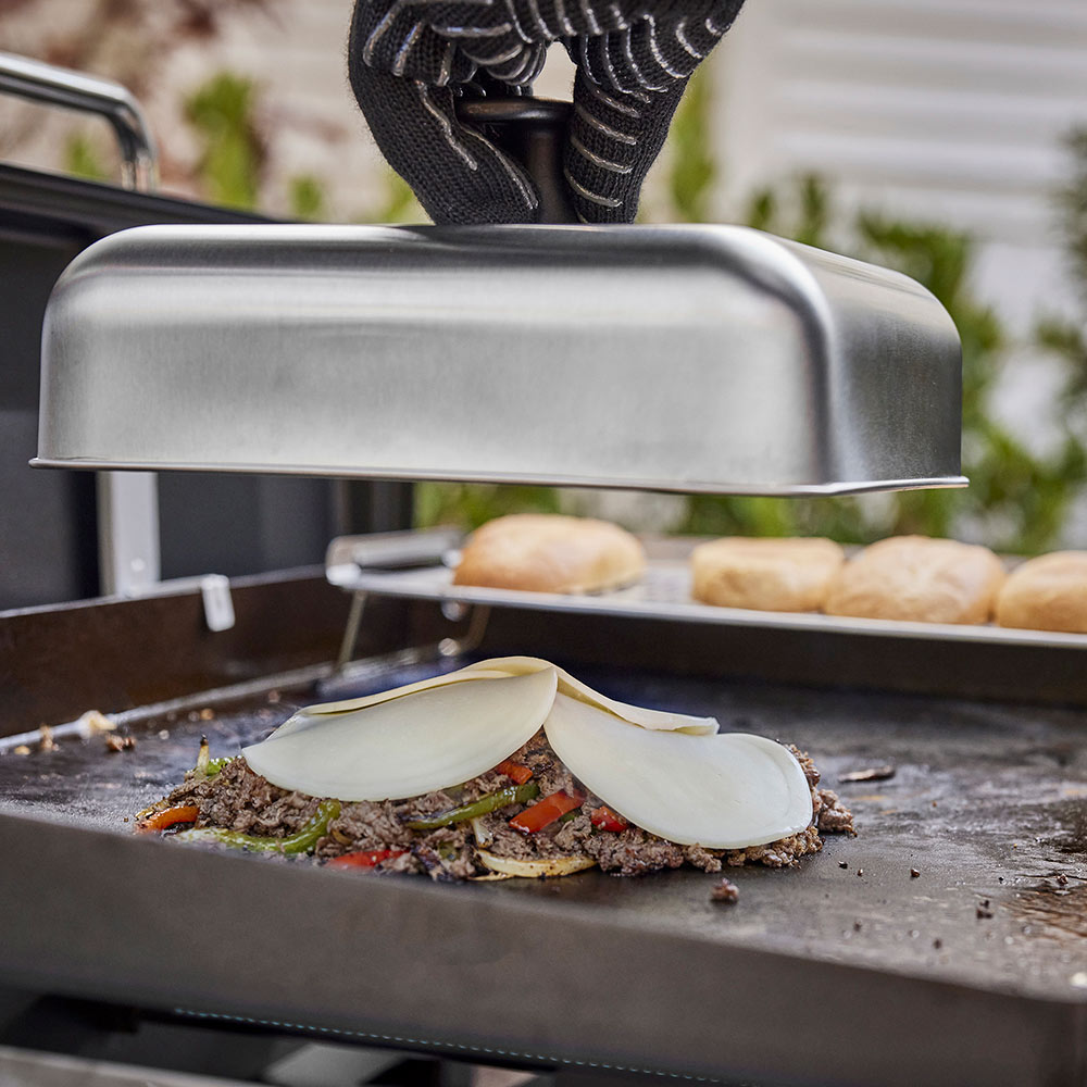 Weber griddle basting dome over grill surface with sliced onions and food