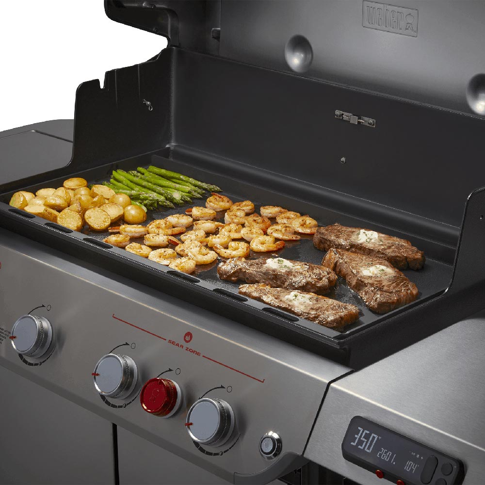Weber griddle on grill with shrimp and steak, plus vegetables on cooking surface