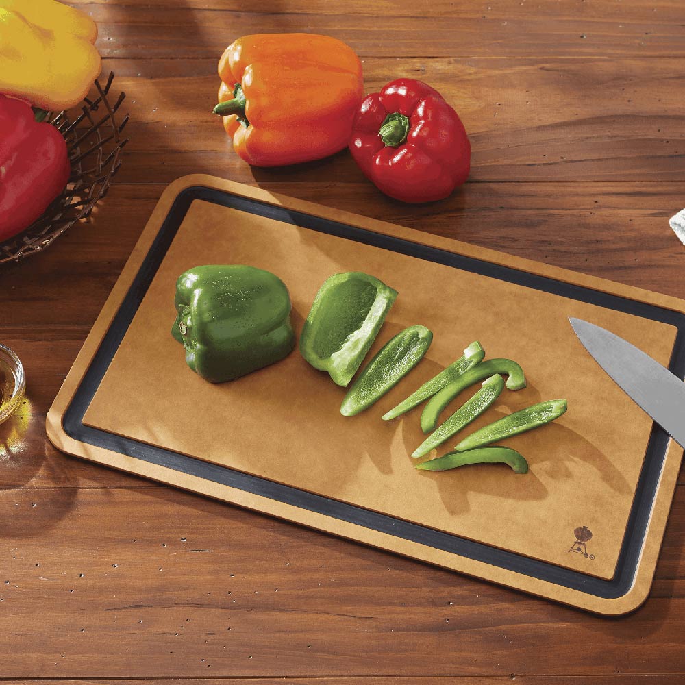 Cutting board with tan surface and dark border, with sliced peppers and a chef’s knife.